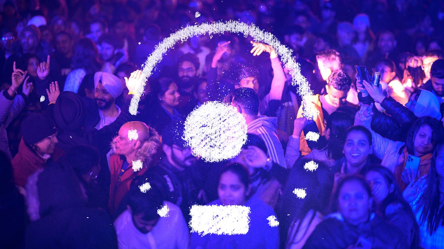 We are looking down at a crowd, lit with purple. A white chalk image hovers above them forming a circle, partially dotted, with a smaller round blob in the middle.