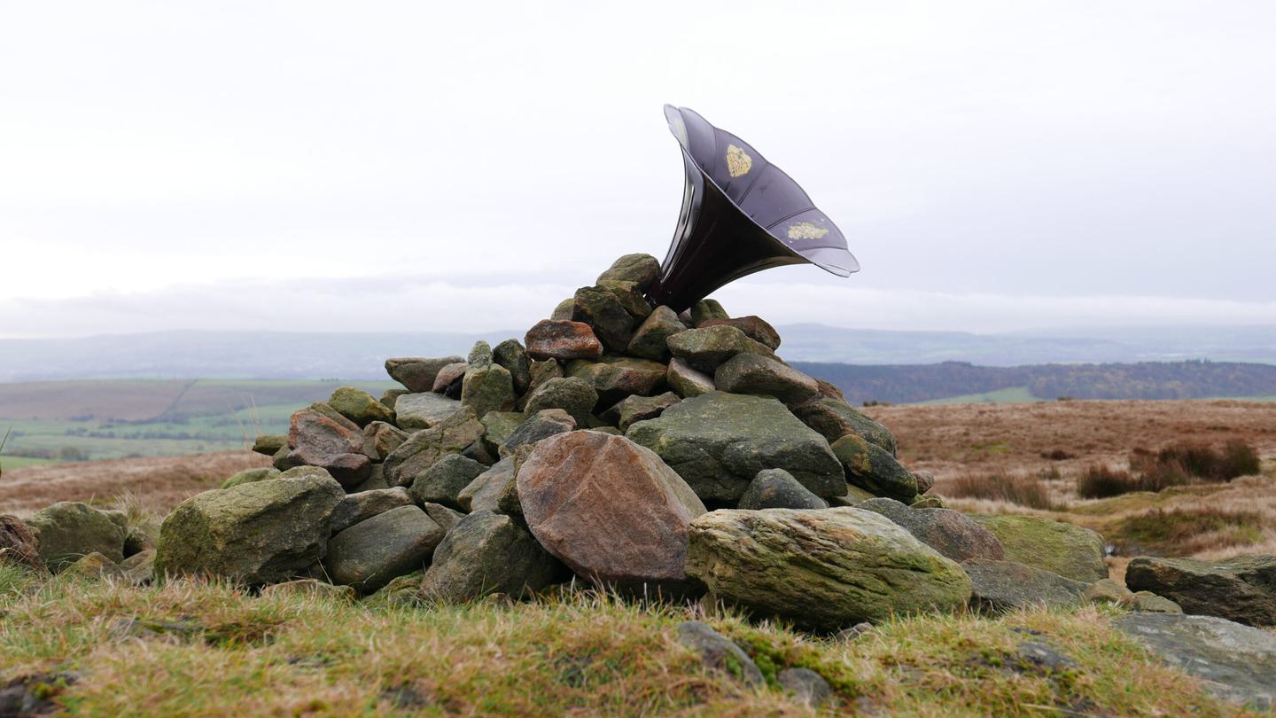 An old style gramophone trumpet points towards the sky out of a rock cairn on top of a hill.