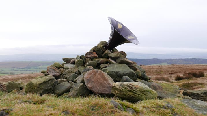 An old style gramophone trumpet points towards the sky out of a rock cairn on top of a hill.